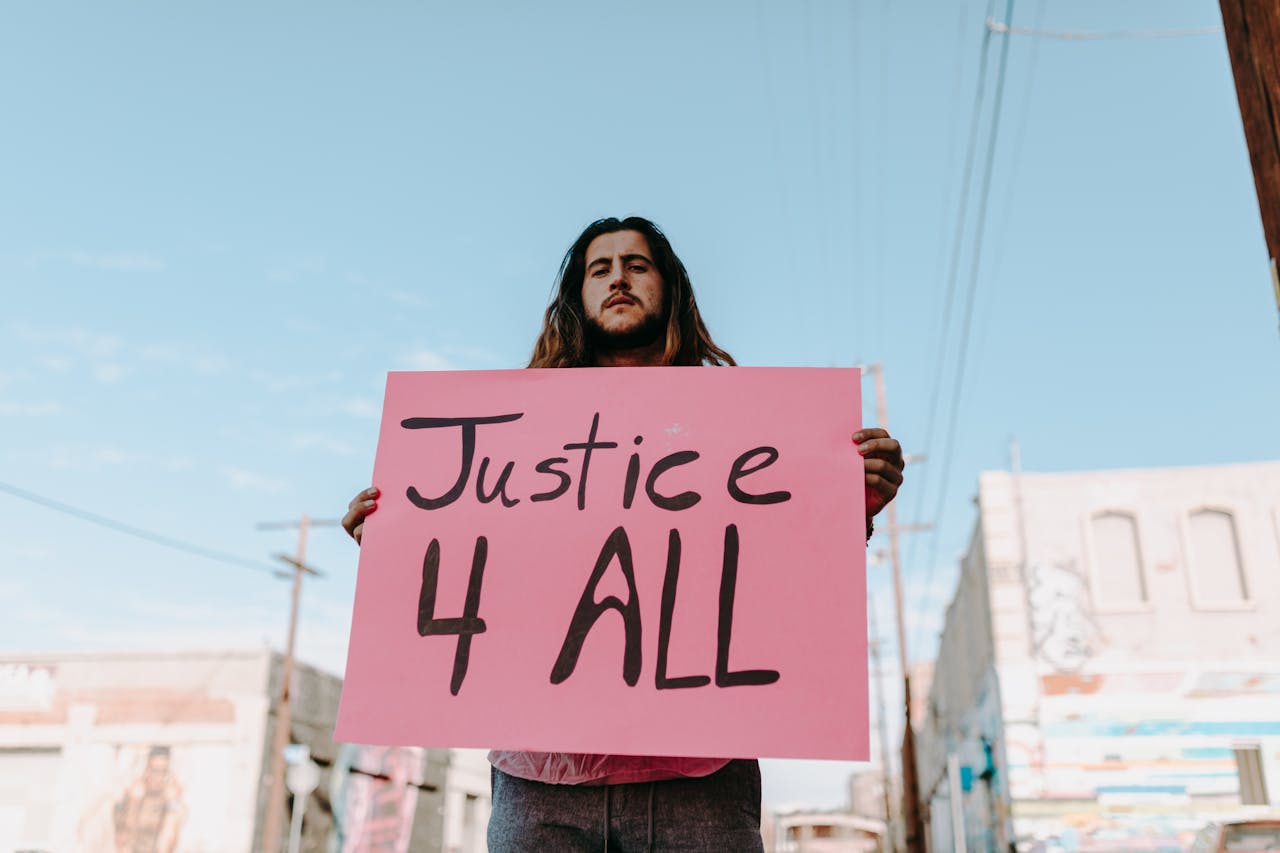 Services-03 Man holding a pink sign reading 'Justice 4 All' at a peaceful protest in an urban setting.